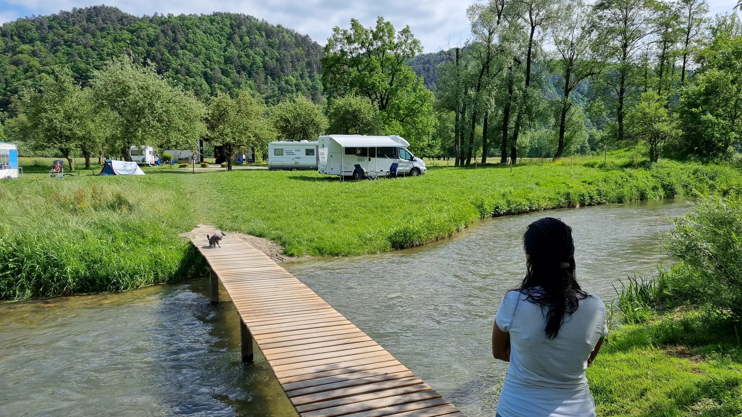Pragya blickt an einem Fluss auf unser Wohnmobil am Campingplatz